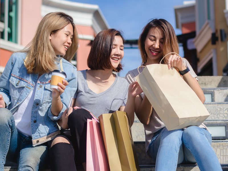 Three friends sitting on steps with shopping bags